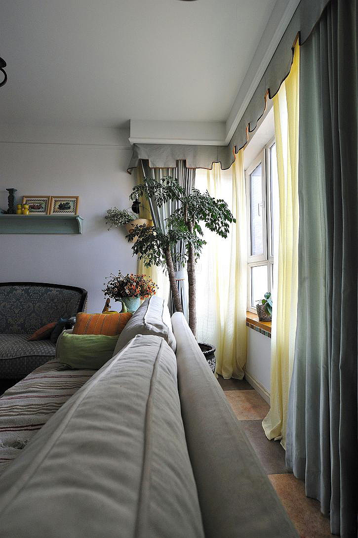 沙发与窗户腾出一段距离，窗边一盆大型绿色植物生长的