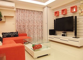 橙红色的沙发和电视墙上方的收纳搁板相呼应